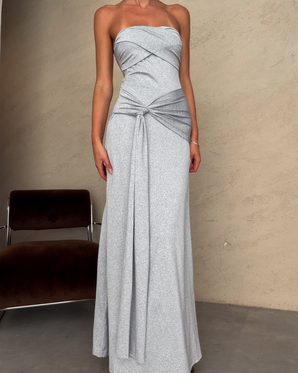 Woman wearing a strapless gray gown with a tie detail against a plain background