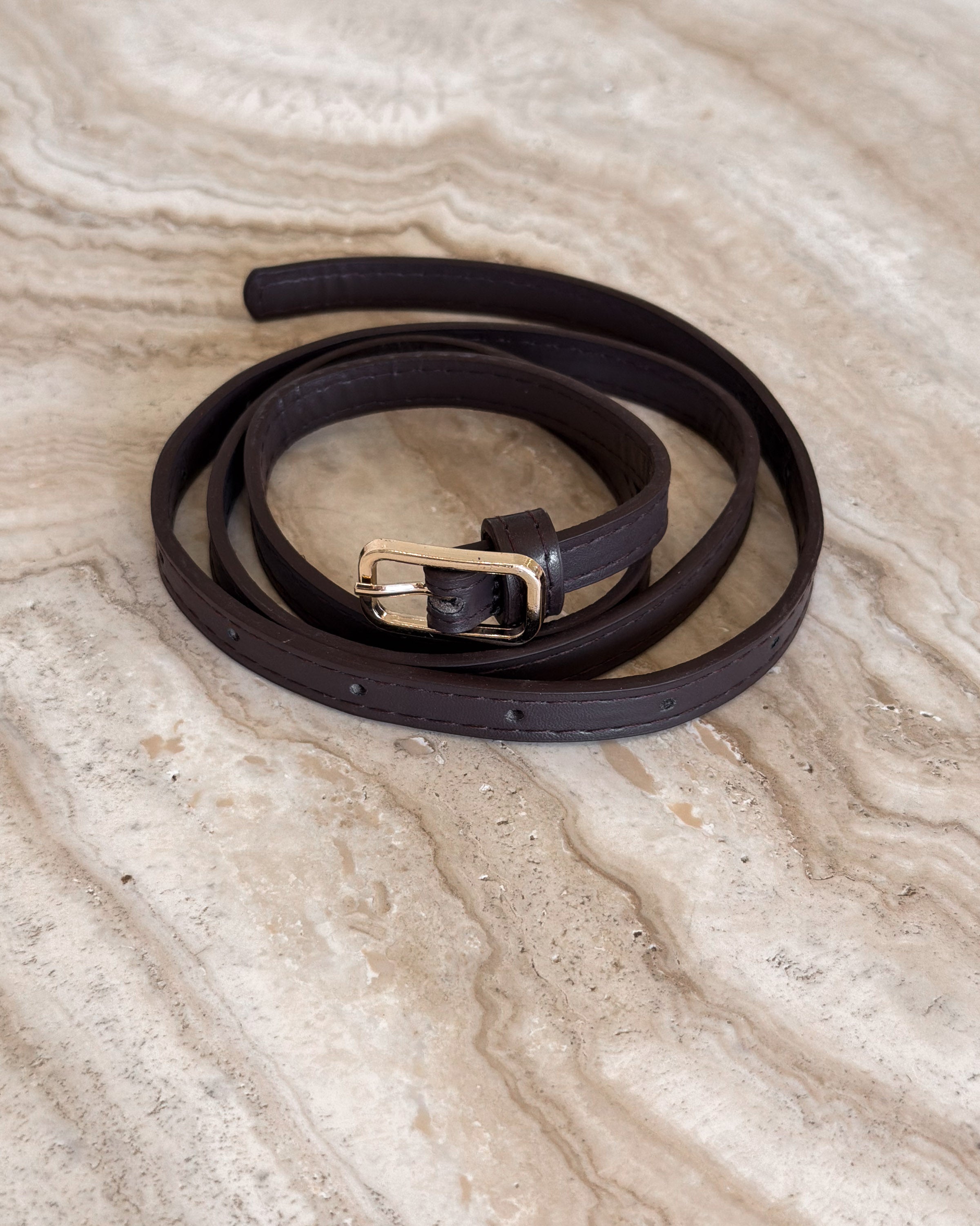 Brown leather belt with a gold buckle on a beige marble surface
