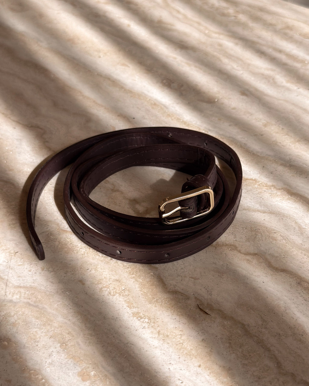 Brown leather belt with a silver buckle on a textured beige surface